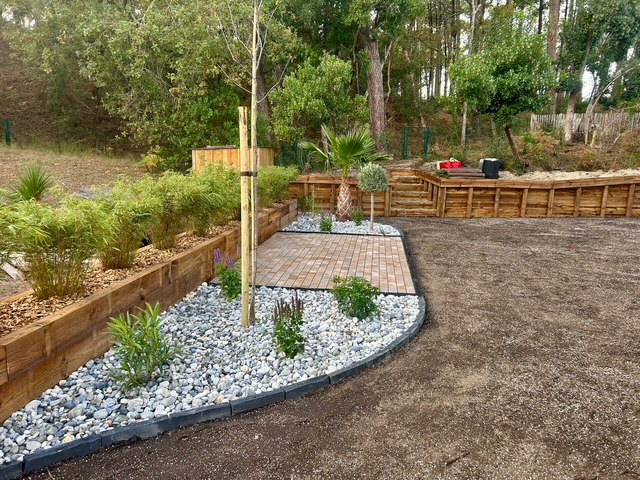 Coin détente extérieur aménagé avec pavés, galets blancs, arbustes persistants et jardinières en bois