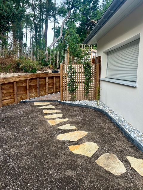 Massif paysager avec palmier, olivier, galets décoratifs et jardinières en bois devant maison moderne