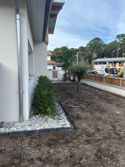 Grand jardin paysager en cours d’aménagement avec clôture en bois, plantations et préparation du sol