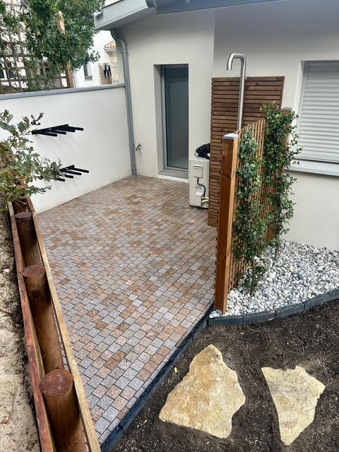 Douche extérieure design avec claustra bois et habillage mural en lames, sur sol pavé dans un aménagement paysager moderne